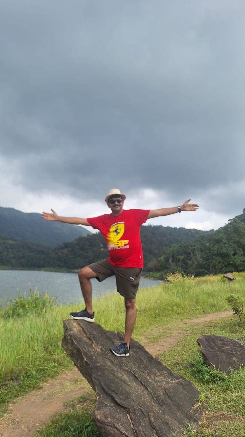 Bipin standing on a rock by a reservoir with hills behind